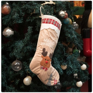 Close-up of beige Christmas stocking with reindeer embroidery hanging on a tree