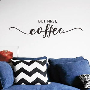 Detail showing 'BUT FIRST, coffee' black wall decal above a blue sofa in a cozy room