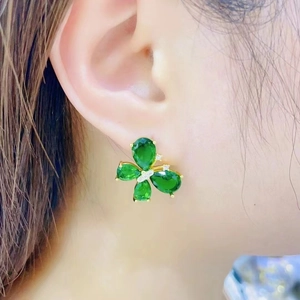 Elegant gold earrings with clover-shaped green gemstones worn by a fashion model