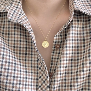 Close-up of gold coin pendant necklace with figure relief on a plaid shirt background