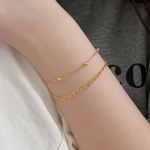 Close-up of double-layer gold beaded bracelet and Figaro chain worn by a model