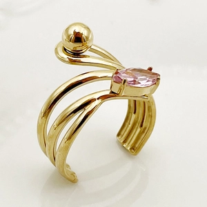 Detail of a golden multi-strand wrap ring featuring a pink gemstone and a gold bead accent