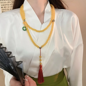 Détail de long collier de perles avec pendentif anneau vert et pompon en soie rouge