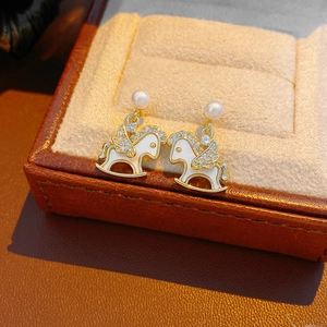 Macro detail of 14k gold plated rocking horse earring with pearl and zircon accents