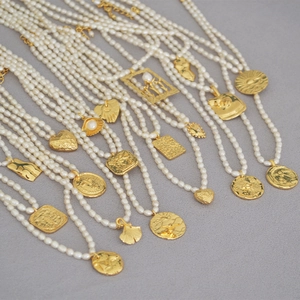 Detailed view of various gold coin pendants and freshwater seed pearls on a choker