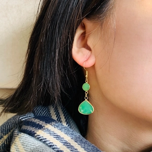 Detail of green teardrop crystal earrings featuring gold metal borders on a female model