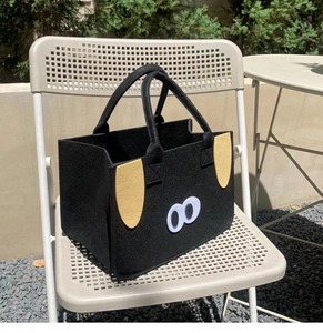 Detail of a black felt tote bag with a cute animal design on a beige metal chair