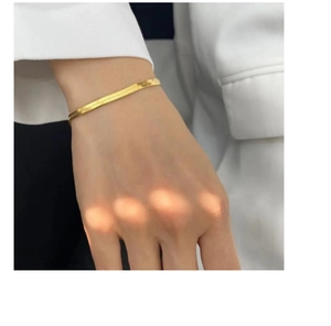 Close-up of a minimalist gold flat snake bone chain bracelet worn on a woman's wrist