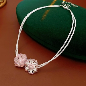 Detail view of double-layered beaded necklace featuring pink flower charms on green velvet