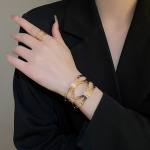 Detailed view of hollow geometric gold bangle and ring set on model with black blazer