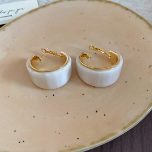 Détail des boucles d'oreilles géométriques en résine plaquée or 18 carats sur un plateau