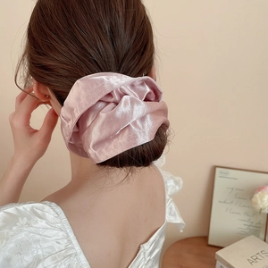 Detail view of a soft pearly pink satin scrunchie with elegant folds and a silky texture