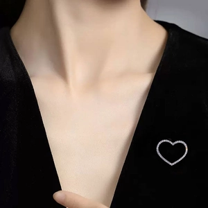 Close-up of a silver heart-shaped brooch with inlaid rhinestones on black velvet fabric