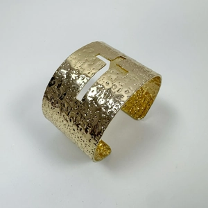 Golden wide open cuff bracelet featuring hammered texture and a central H-shaped cutout