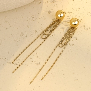 Detail view of gold tassel earrings with long metallic chains on a beige stone surface