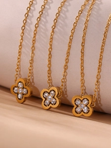 Macro detail of 18k gold plated clover necklaces with white zircon stones on beige fabric