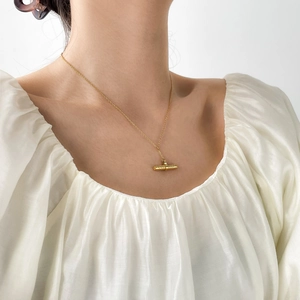 Close-up of gold plated stainless steel cylindrical pendant necklace on a model