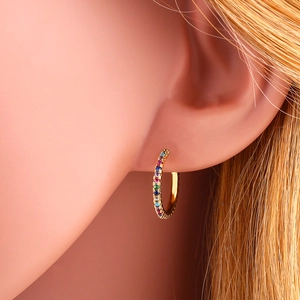 Close-up of golden huggie earrings with a row of vibrant rainbow zircon stones