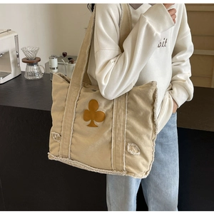 Detail of beige corduroy tote bag with frayed edges and brown club spade patch