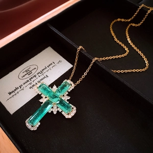 Détail du pendentif croix avec zircons carrés verts et texture de chaîne dorée