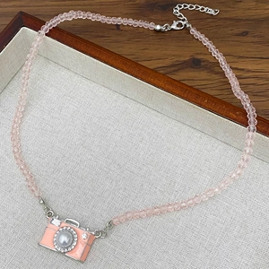 Roze camera hanger ketting met kristallen kralen en parel op een sieradenblad