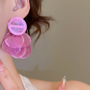 Close-up of a woman wearing pink shell-textured circular tassel earrings for vacation style