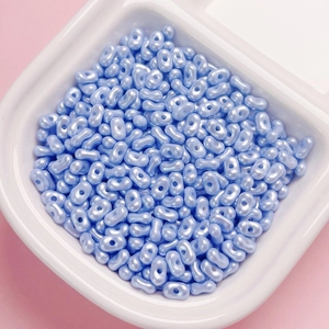 Macro detail of light blue pearlescent peanut beads in a white bowl for DIY jewelry