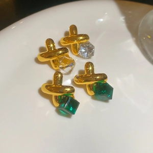Macro detail of gold cross earrings with clear and emerald green crystal cubes