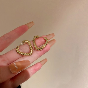 Makroaufnahme vergoldeter herzförmiger gedrehter Ohrringe mit Vintage-Metalltextur