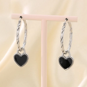 Detail of twisted silver hoop earrings with black enamel heart charm on a display stand