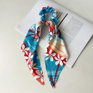 Detail view of a tropical floral satin scrunchie with long ribbons on an open magazine