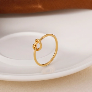 Minimalist gold knot ring in stainless steel displayed on a white ceramic plate