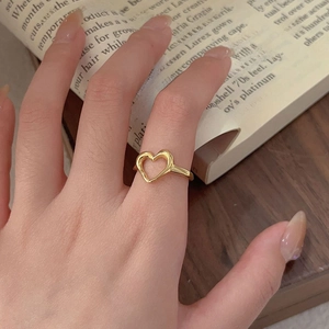 Minimalist gold heart ring shown on model's hand resting over a vintage book page