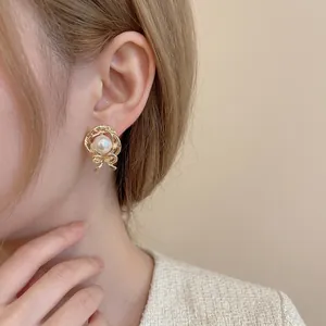 Elegant gold bow earrings with pearls and hollow metal design worn by a female model