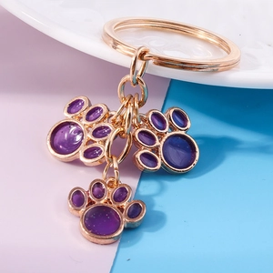 Detailed close-up of golden metal cat paw keychain with purple enamel charms on a split background
