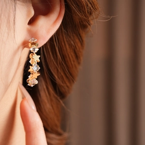 Close-up of sparkling star-shaped zircon C-shaped earrings worn by a model in gold finish