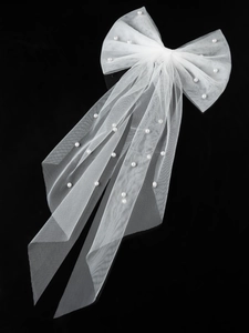Detail of white tulle bridal bow hair clip with scattered pearls on black background