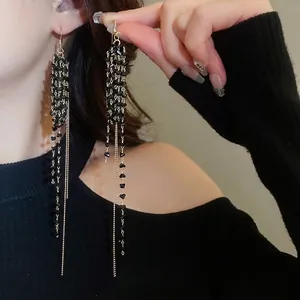 Orecchini lunghi con perle di vetro nere e nappine dorate indossati da una modella
