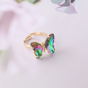 Detalle de anillo dorado ajustable con mariposa degradada y cristales iridiscentes