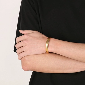 Bracciale a fascia aperta a C in acciaio al titanio dorato indossato al polso di una donna