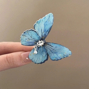 Detail of blue butterfly hair clip with shimmering rhinestones and a white pearl drop