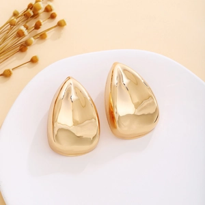 Detail view of golden waterdrop earrings with a polished metallic finish on a ceramic plate