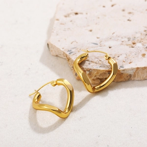 Detail of gold-plated wavy twisted hollow earrings resting on a textured light stone