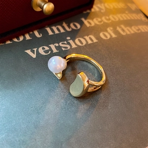 Minimalist gold-plated open ring featuring a white pearl and bean-shaped accent on a magazine
