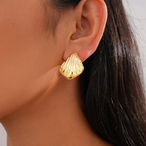 Close-up of model wearing golden textured oval stud earrings with wave pattern details