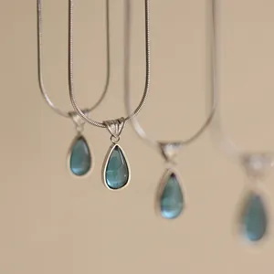 Detail of blue teardrop pendants with translucent stones and silver snake chain necklaces