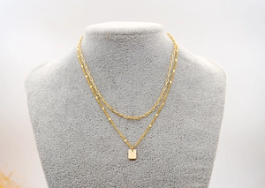 Close-up of double-layer gold necklace featuring paperclip chain and Good Luck tag