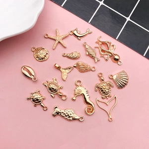 Flat lay of 15 gold marine animal charms including starfish and shells on pink background