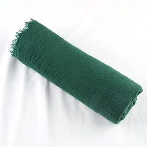 Detail of dark green cotton linen scarf with frayed edges and natural crinkle texture