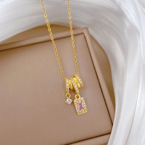 Detail of a gold cross chain necklace with pink square zircon on a beige jewelry box